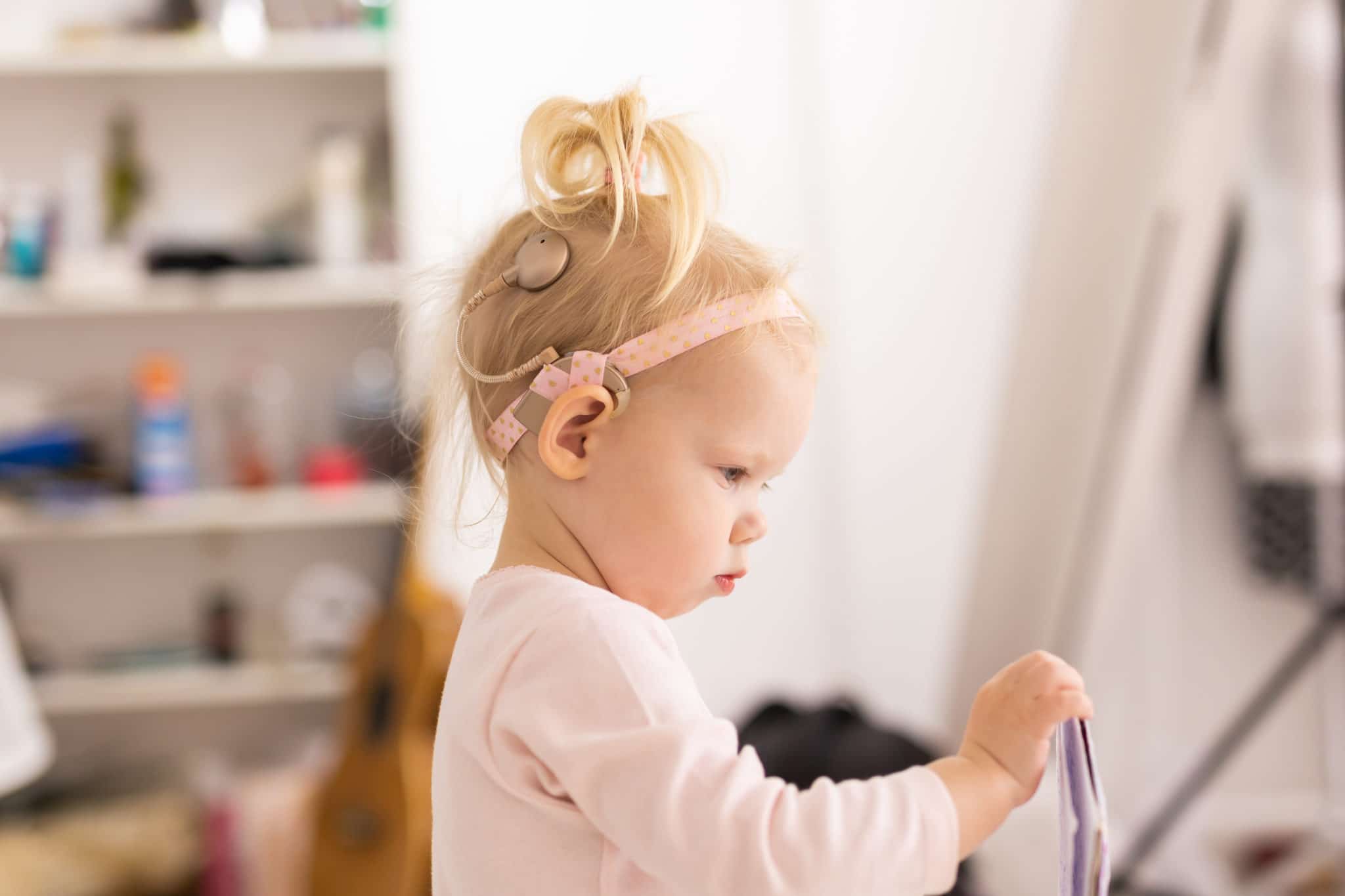 baby with cochlear implants having fun at home. deafness and medical technology concept.